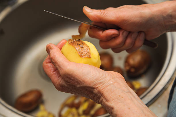 Elderly woman to peel potatoes. Kitchen working. Prepare food stock photo