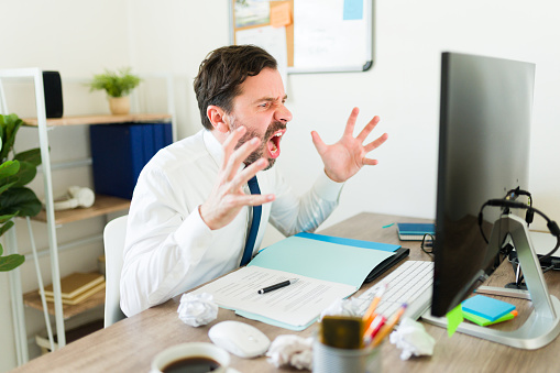 Angry businessman laywer or boss screaming while having work problems and looking at his computer screen yelling looking upset