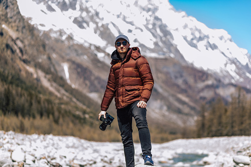 Photo of a caucasian tourist man with digital camera for photography. Person is photographer, guy is photographing with DSLR for work. Traveling concept picture, beautiful nature and landscape in the mountains