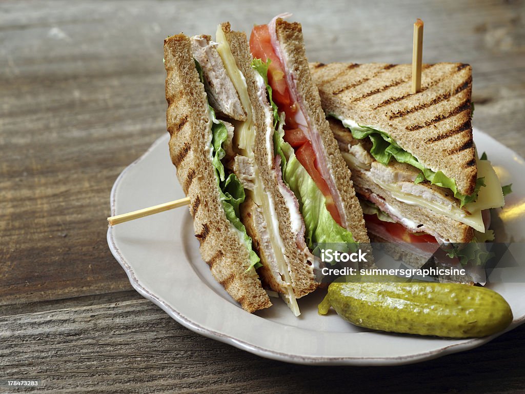 Club sandwich on a plate Photo of a club sandwich made with turkey, bacon, ham, tomato, cheese, lettuce, and garnished with a pickle. Club Sandwich Stock Photo