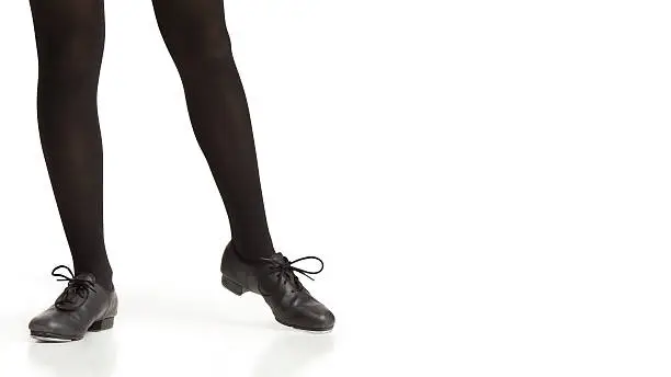 Studio image isolated on white of a young girl's legs in black tights and tap shoes dancing.