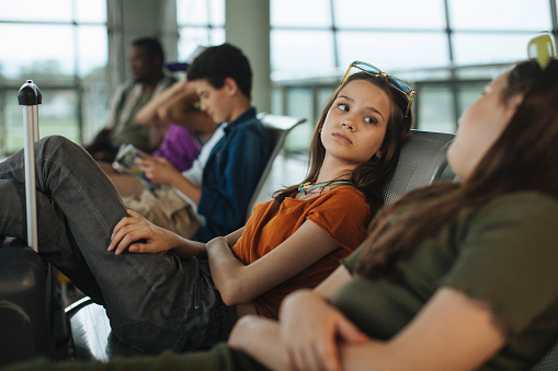 At the airport waiting area, a cluster of teens relaxes in their seats, engaged in lively conversation