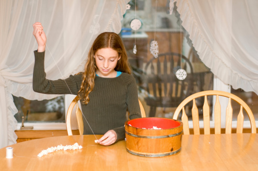 young Caucasian girl stringing popcorn to make Christmas decorations