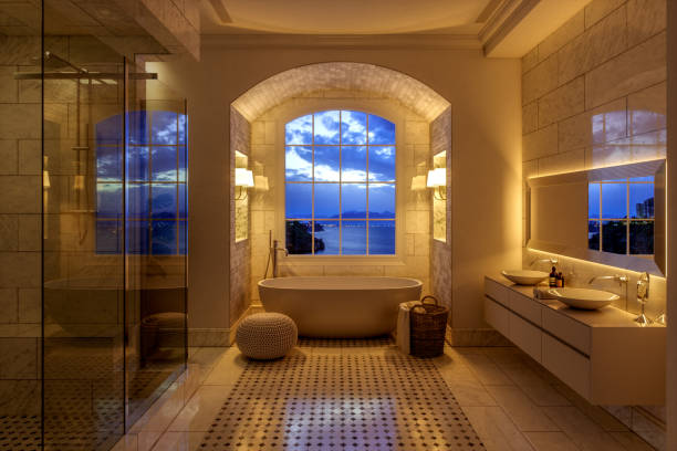 Interior of a warm lit contemporary white bathroom with washstand and bathtub at night.