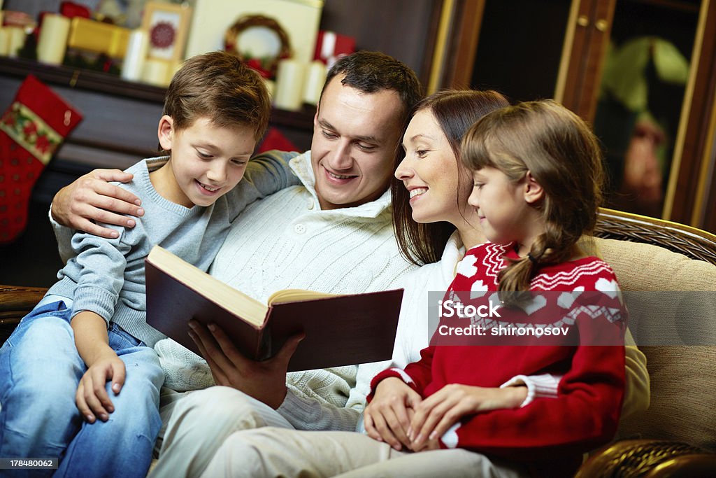 Family reading Portrait of friendly family reading book on Christmas evening Adult Stock Photo