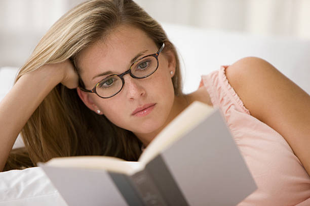 Beautiful young woman reading a book on bed