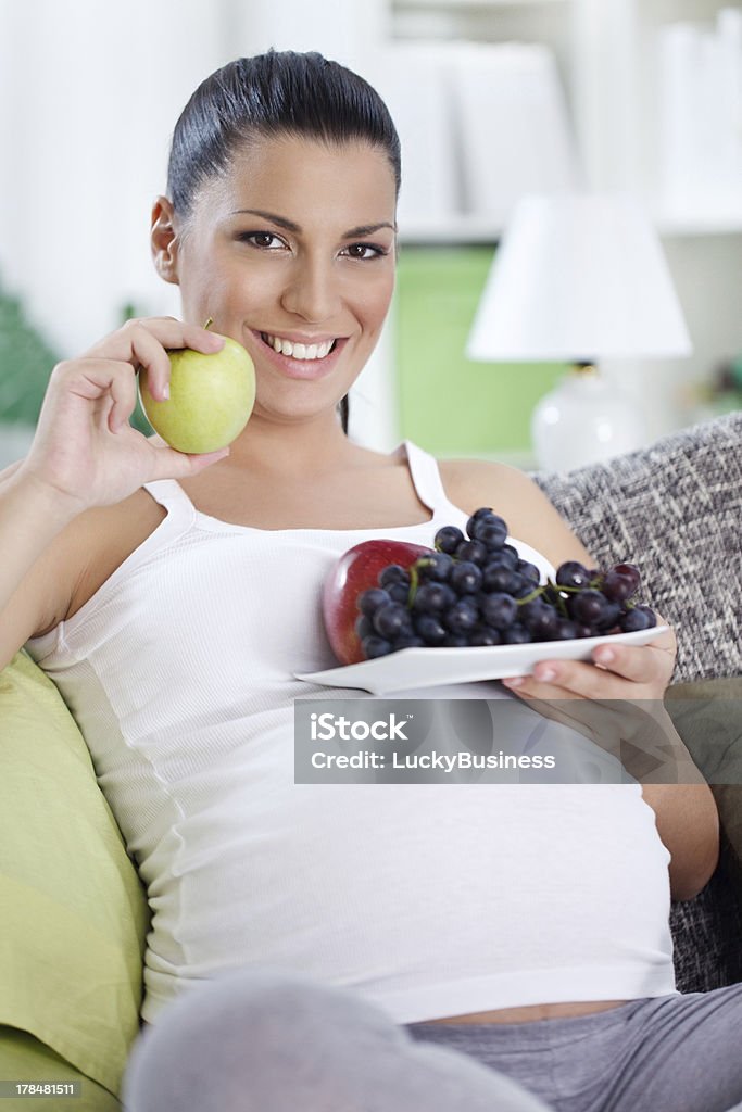 Pregnant woman eating fruits "Pregnant woman eating fruits, holding plate with fruits in belly" Abdomen Stock Photo