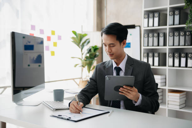 istock Young handsome man typing on tablet and laptop while sitting at the working wooden table modern office 1784865649