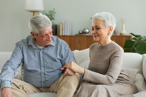 Senior adult mature couple in love holding hands at home. Mid age old husband and wife looking with tenderness love enjoying wellbeing. Grandmother grandfather together. Family moment love and care