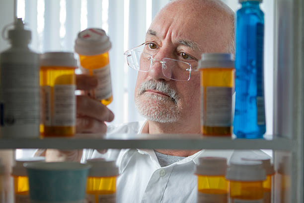 senior hombre estudiando los medicamentos recetados - armario de aseo personal fotografías e imágenes de stock