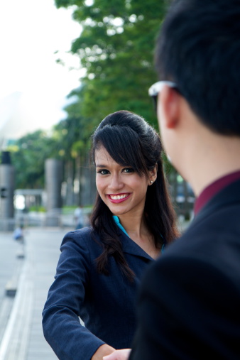 Smiling female asian business executive shaking hands with her male colleague outdoors.