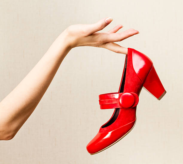 Female hand holding red varnish shoes on a high heel stock photo