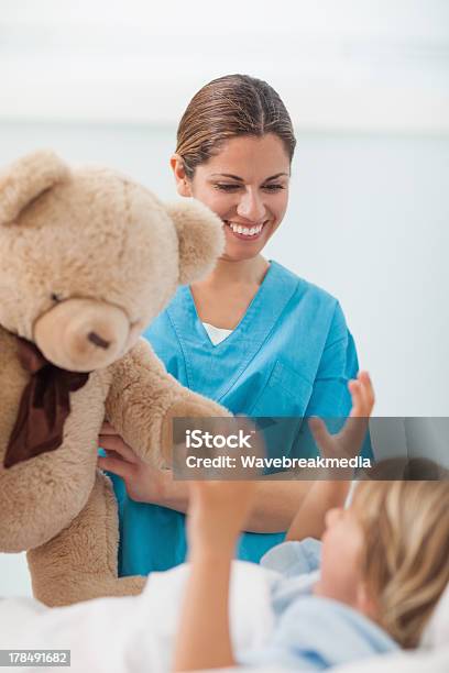 Sorridente Enfermeira Mostrando Urso De Pelúcia Para Uma Criança - Fotografias de stock e mais imagens de Criança