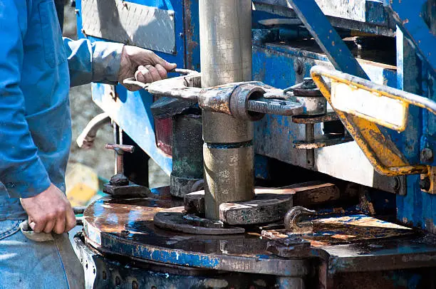 A worker uses a large wrench to screw on a drill casing during the operation of a water well drill rig.