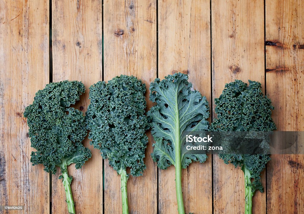 Four pieces of kale one turned over on a wooden background "Kale or borecole (Brassica oleracea Acephala Group) is a vegetable similar to cabbage, with green or purple leaves, in which the central leaves do not form a head." Beta Carotene Stock Photo