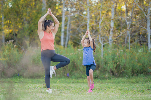 A young Mother of Asian decent stands outside with her daughter as they practice Yoga in the fresh air.