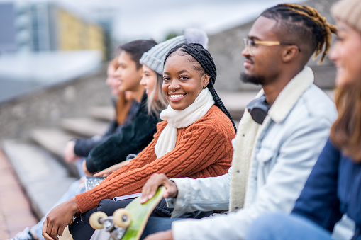 A small group of University students of various ethnicities, sit together on a set of stairs as they casually carry conversations and get to know one another.