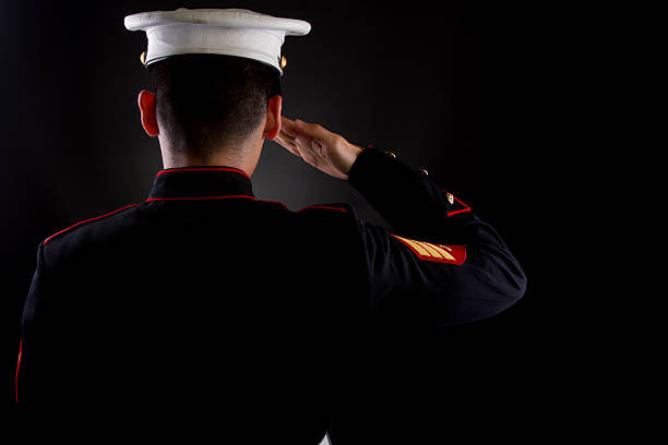 Marine saluting in dress blues A U.S. Marine saluting against a black background while in the dress blues service uniform. military deployment photos stock pictures, royalty-free photos & images