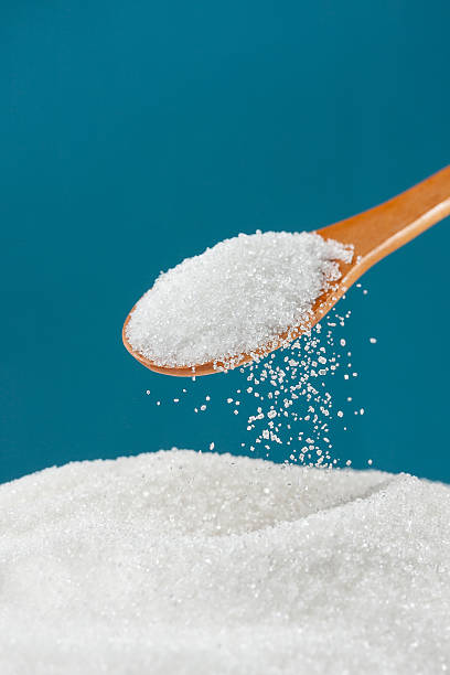 Closeup view of sugar falling from a spoon into a pile stock photo