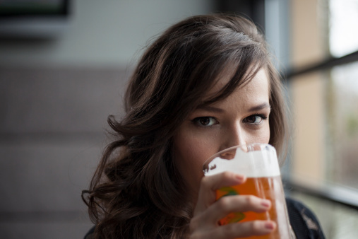 Portrait of a young woman drinking a pint glass of beer.
