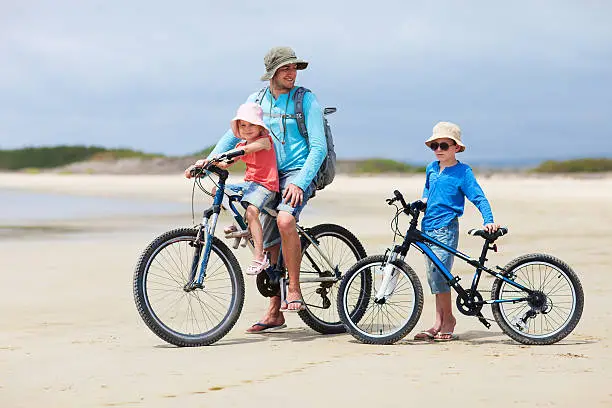 Father and kids riding bikes along a beach