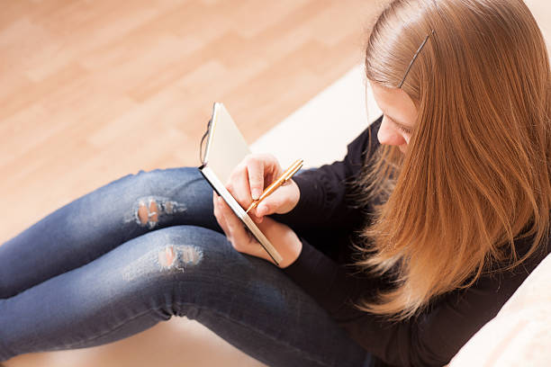 istock Happy teen writing to the diary sitting on sofa 178500455