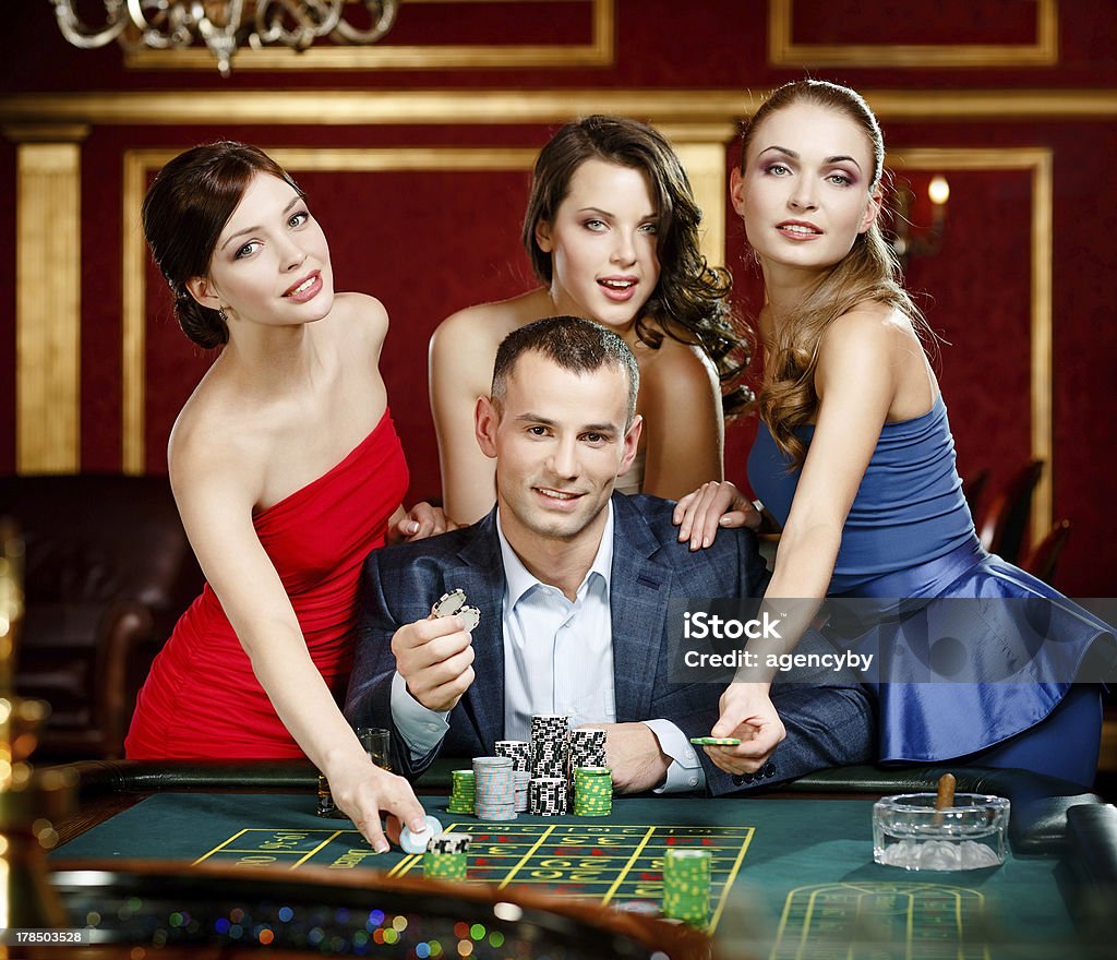 Man surrounded by girls gambles roulette Man surrounded by women plays roulette at the casino club Activity Stock Photo