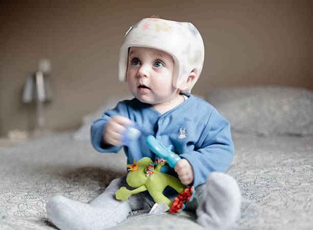 cute baby boy 6 months old looking at camera. He is wearing a helmet to corect plagiocephaly