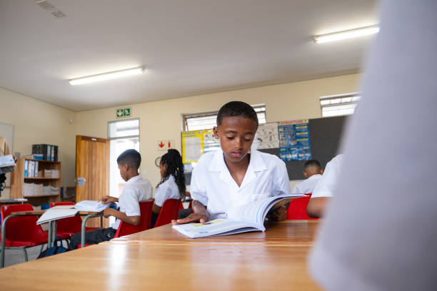 A group of young black children from a rural school in South Africa sit in class with their books open going through their work together in small study groups