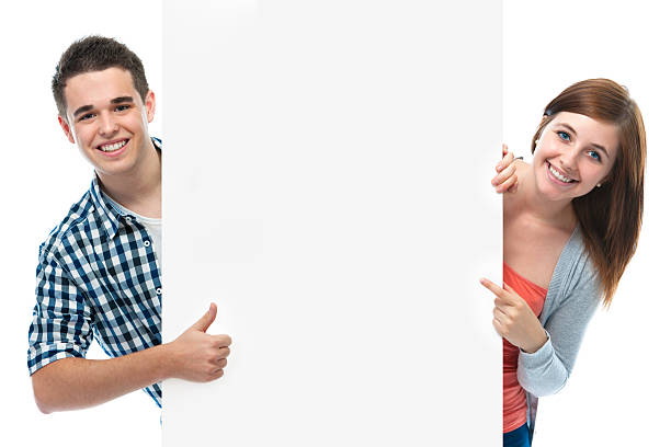 two smiling teenagers holding at a blank board