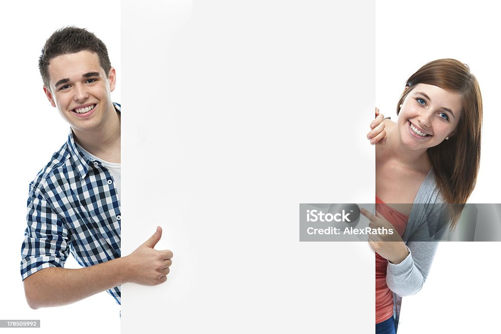 Smiling teenagers behind white wall two smiling teenagers holding at a blank board Teenager Stock Photo