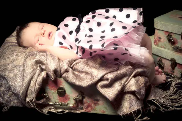 Cute baby girl wearing a dress sleeping in a suitcase