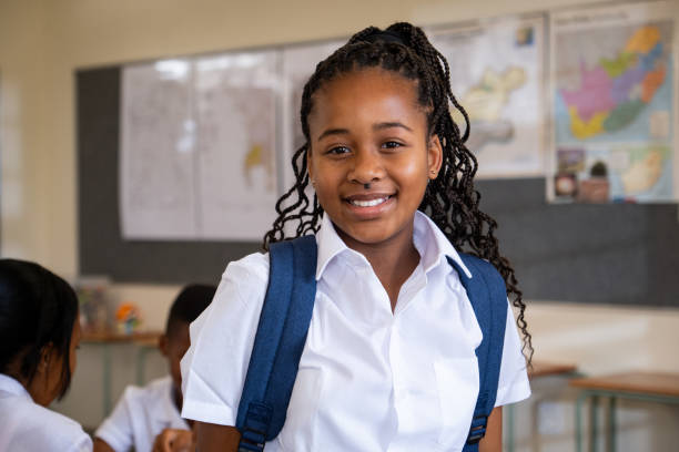 Portrait of a young black schoolgirl with curly black hair A close up portrait of a young African schoolgirl with long black curly hair and her schoolbag over her shoulders. black african girls pictures stock pictures, royalty-free photos & images