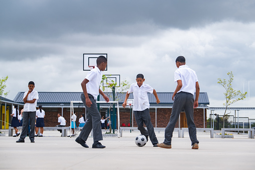 A small group of schoolboys enjoy a friendly soccer game in the school yard. Black boys in a rural school play soccer during the lunch break at school