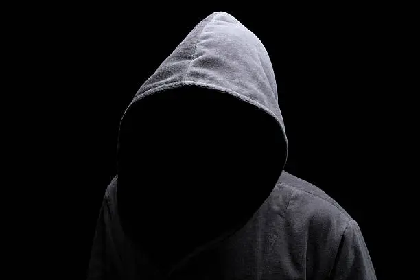 Menacing silhouette of hooded man in the shadow isolated on black background