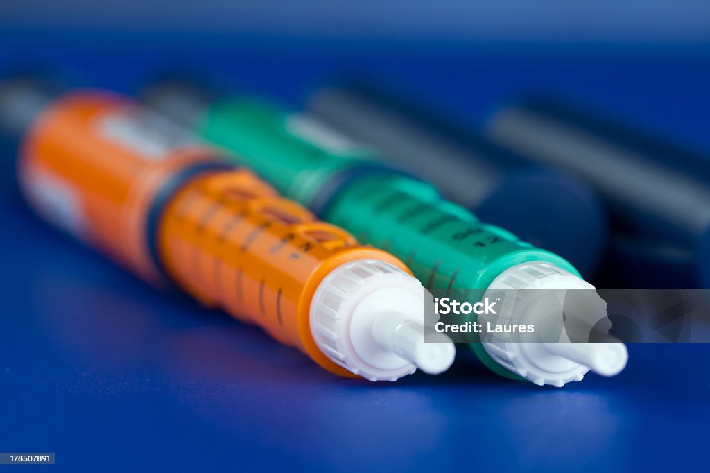 Close up of green and orange insulin syringe pens Two insulin syringe pen on a blue background Insulin Stock Photo