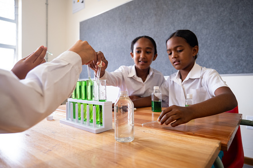 A group of schoolgirls enjoy a fun science experiment as past of their lesson. They are mixing various liquids to see the different reactions they have.