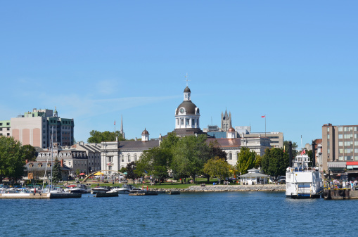 This photo shows City Hall in the City of Kingston Ontario Canada from the water.  It shows the trees and fountain in Confederation Park in front of the domed City Hall building.  The dome also has a clock and bell tower.  A marina with boats is in front of the park also.  A large tour boat sits waiting for tourists to tour the Thousand Islands.  Kingston is on Lake Ontario where the St. Lawrence and Rideau Rivers meet.