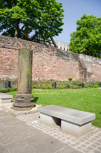 A stone bench and sandstone pillar can be seen in the foreground with the old Roman walls and part of the Nine Houses in the background.