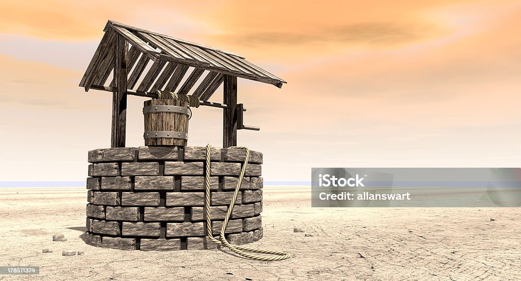 Wishing Well With Wooden Bucket On A Barren Landscape A brick water well with a wooden roof and bucket attached to a rope in a flat barren landscape with an orange sky Arid Climate Stock Photo
