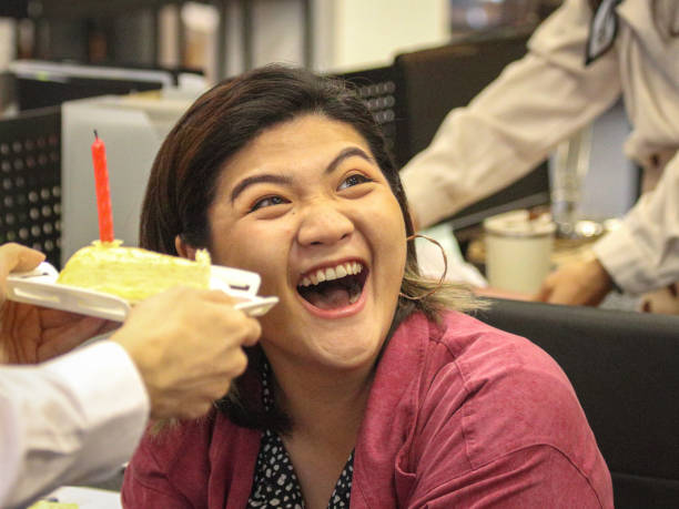 азиатская офисная работница, работающая в офисе, была приятно удивлена, когда коллега неожиданно подарил ей праздничный торт. - office fun group of people white collar worker стоковые фото и изображения