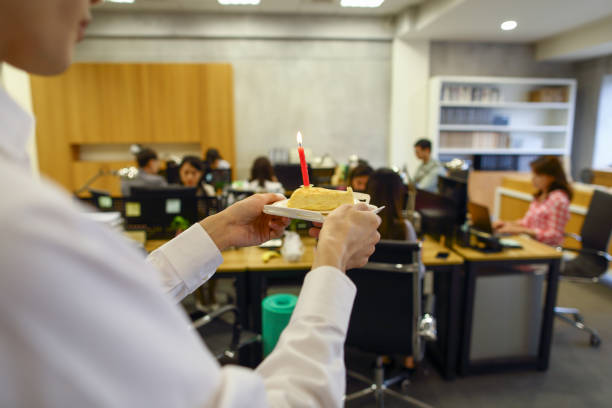 азиатский мужчина, служащий «белых воротничков», несет простой нарезанный торт, чтобы удивить своего коллегу, у которого сегодня день рожд� - office fun group of people white collar worker стоковые фото и изображения
