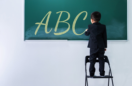 A boy writing letters a, b, c on chalkboard