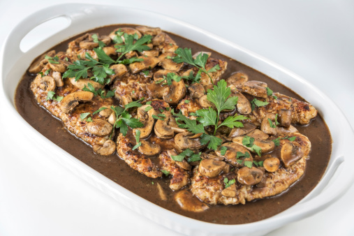 A white platter full of Chicken Marsala topped with fresh parsley sits on a white background.  Room for copy space in 2 corners.