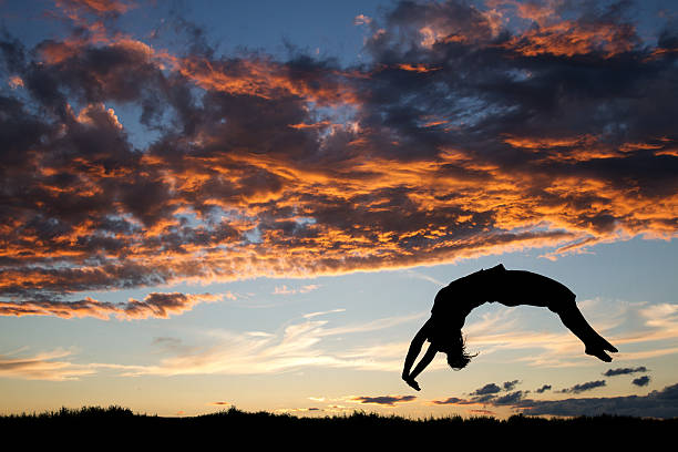 gymnast in sunset doing a back handspring silhouette of gymnast in sunset doing a back handspring on grass handspring stock pictures, royalty-free photos & images