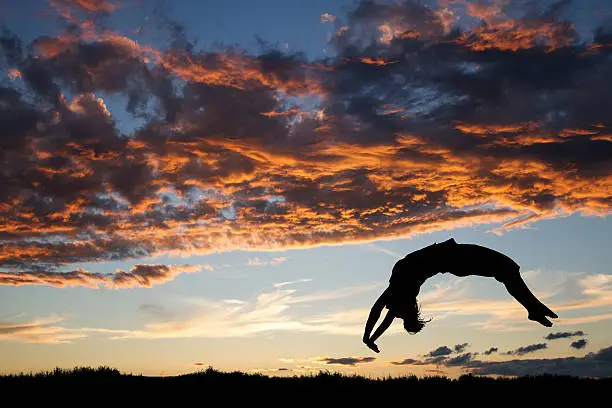 silhouette of gymnast in sunset doing a back handspring on grass