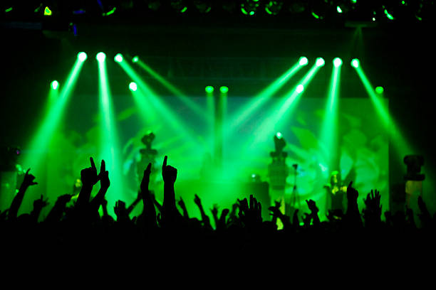 A crowd at a concert waving their hands with green lights in the background.