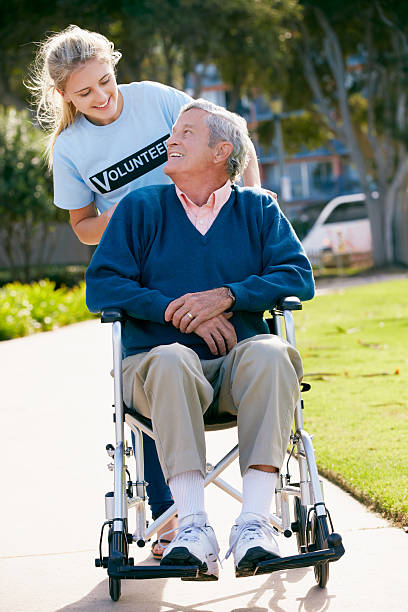 adolescente senior hombre empujando voluntarios para silla de ruedas - care community 80 plus years cheerful fotografías e imágenes de stock