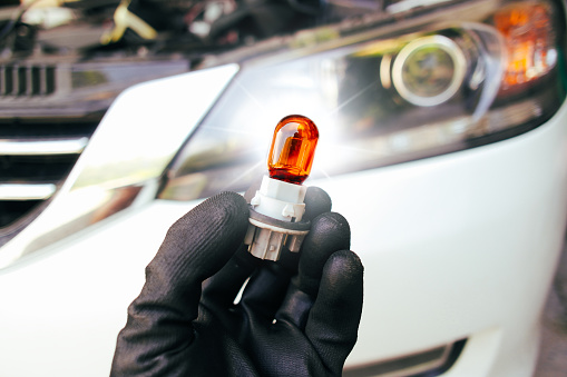 Orange turn signal light bulb in auto mechanic hand with a car blurred background , T20 type , Car parts concept