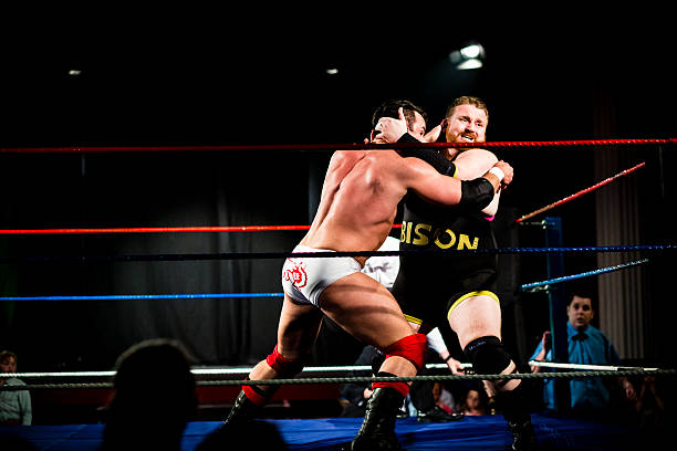 Wrestlers in combat Wrestler in the ring with strangle hold on another wrestler. Compare can be seen looking on in background wrestling stock pictures, royalty-free photos & images